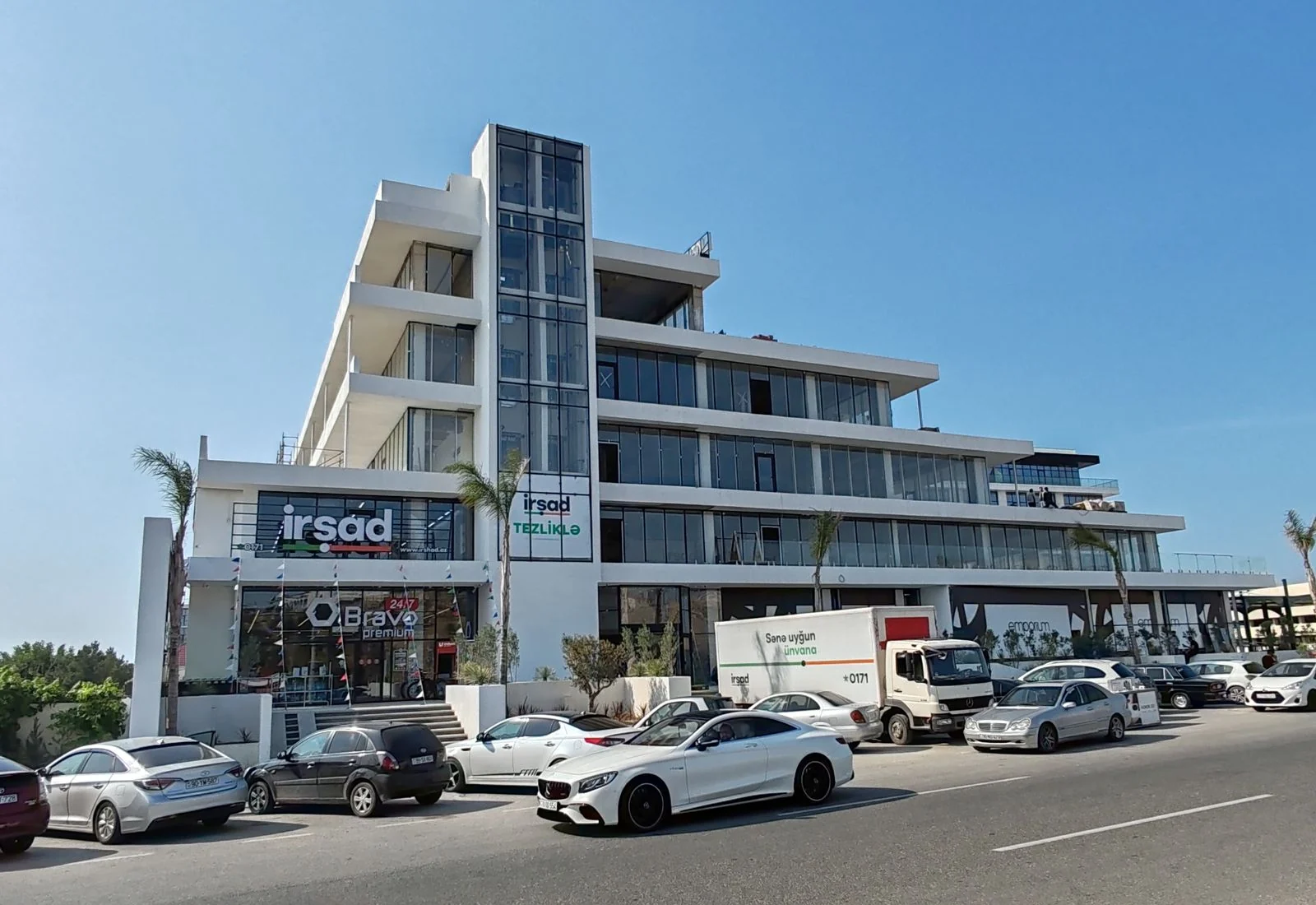 Lighthouse Mall за две недели до открытия: вывеска İrşad на втором этаже, под ней Bravo Premium 24/7, на стеклянной шахте — баннер «İrşad · Tezliklə» («скоро»)
